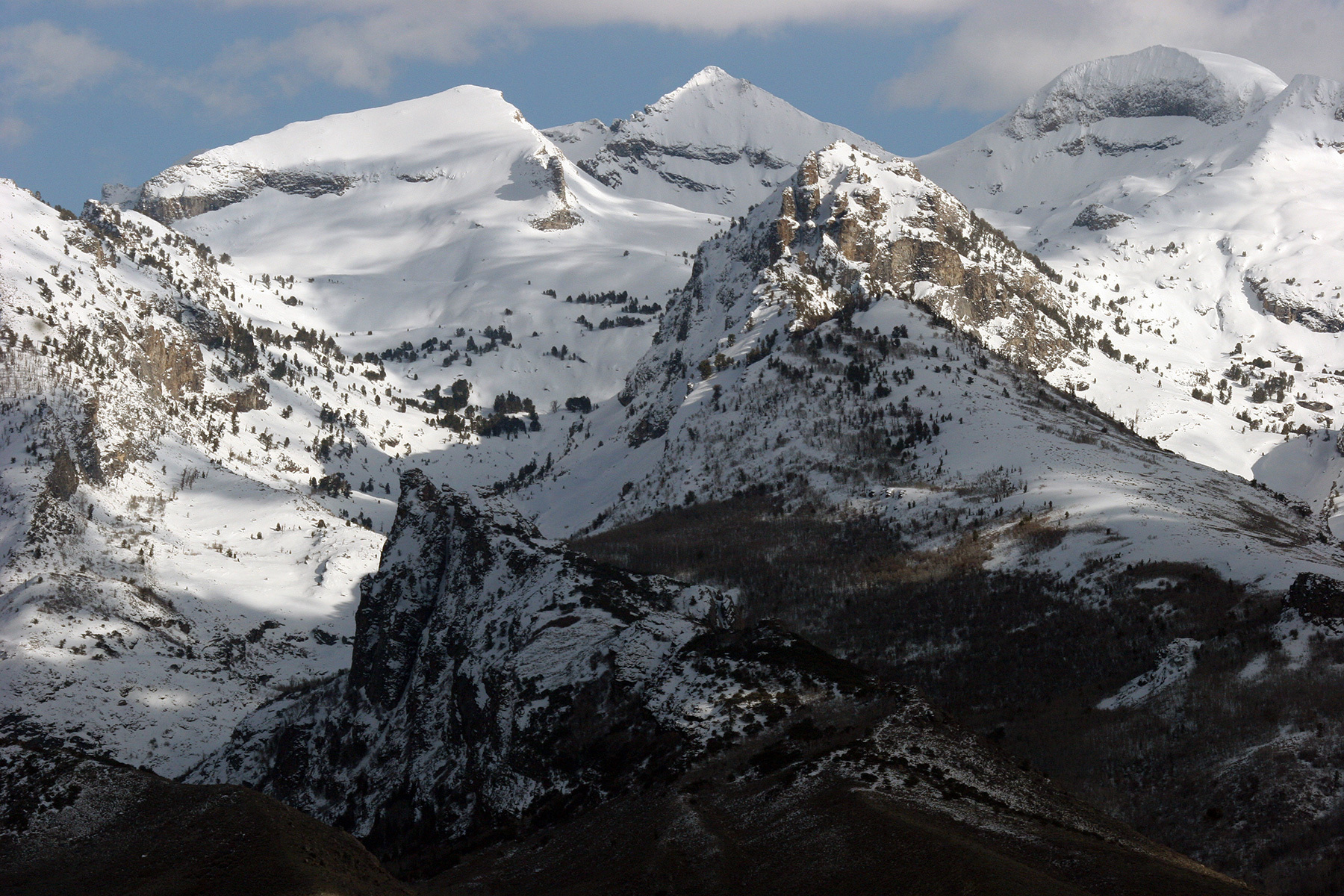 Auto-generated description: Snow-covered mountains with rugged peaks under a partly cloudy sky.